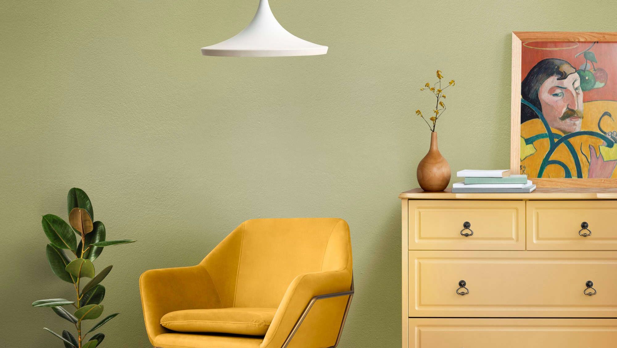 Grønnmalt vegg med gul stol, kommode og moderne interiørdetaljer.