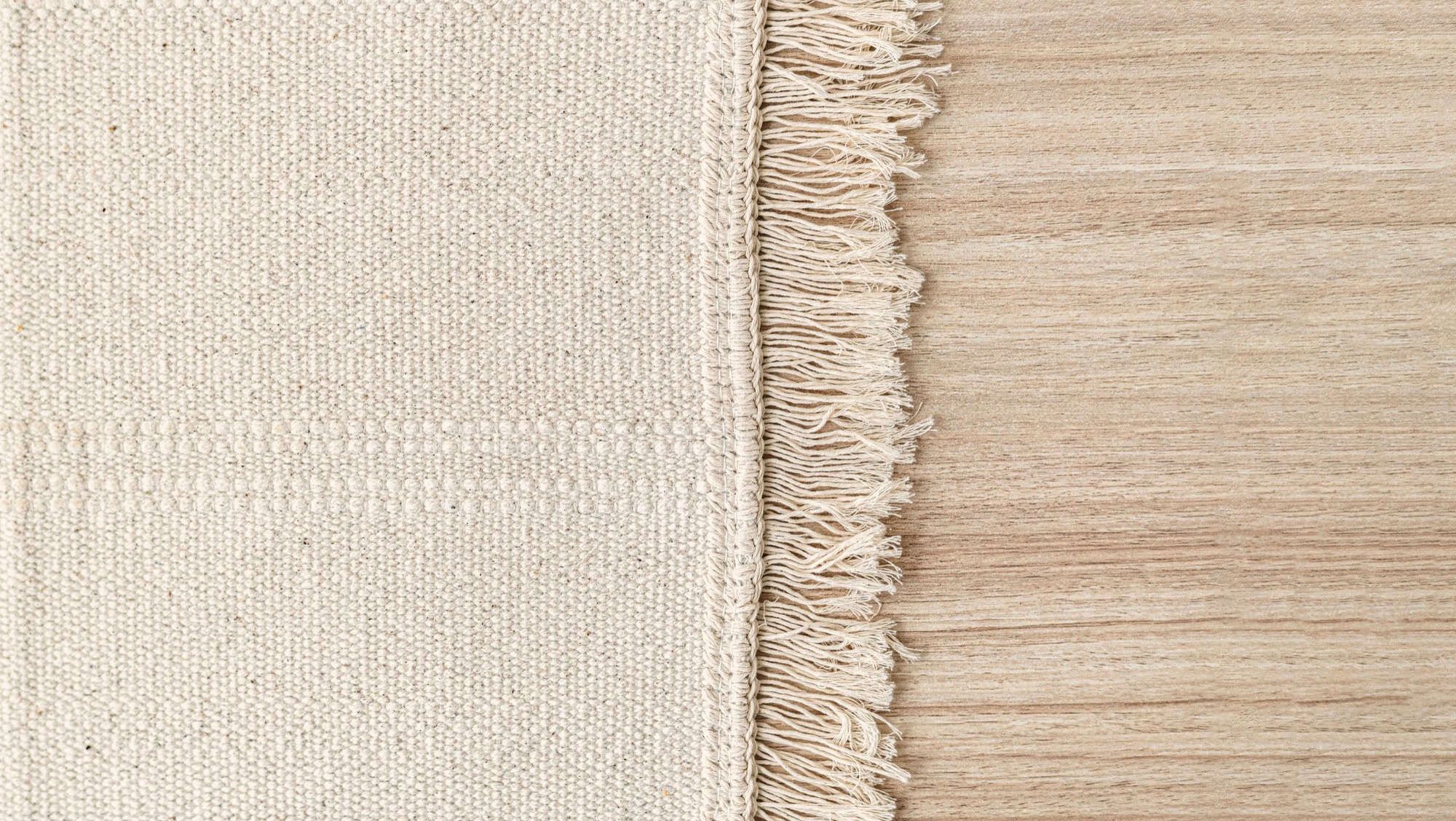 Lysvevd teppe med frynser delvis lagt på tregulv.