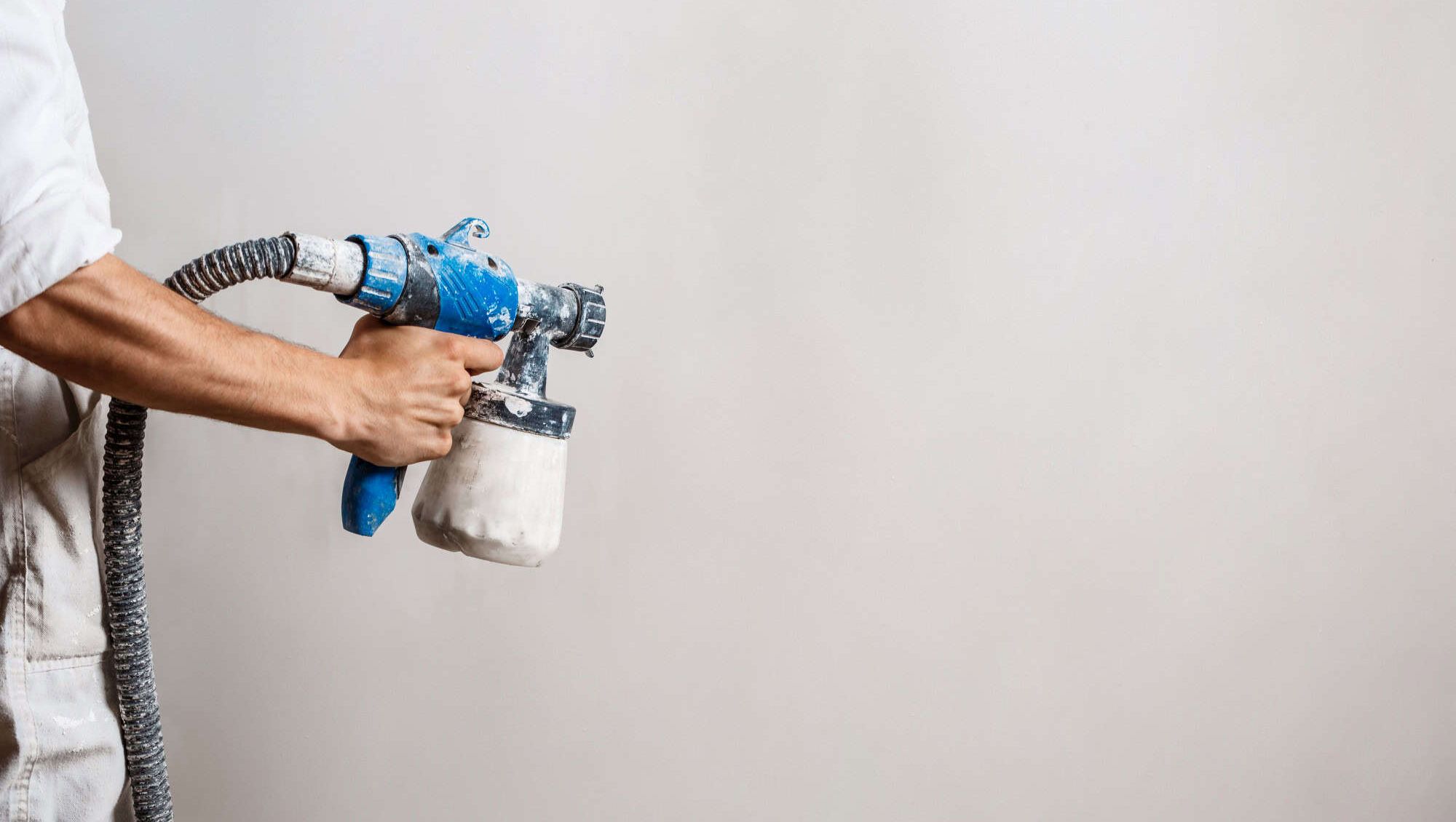 En maler sprøyter maling på en vegg med en blå og hvit malingssprøyte i nærbilde.