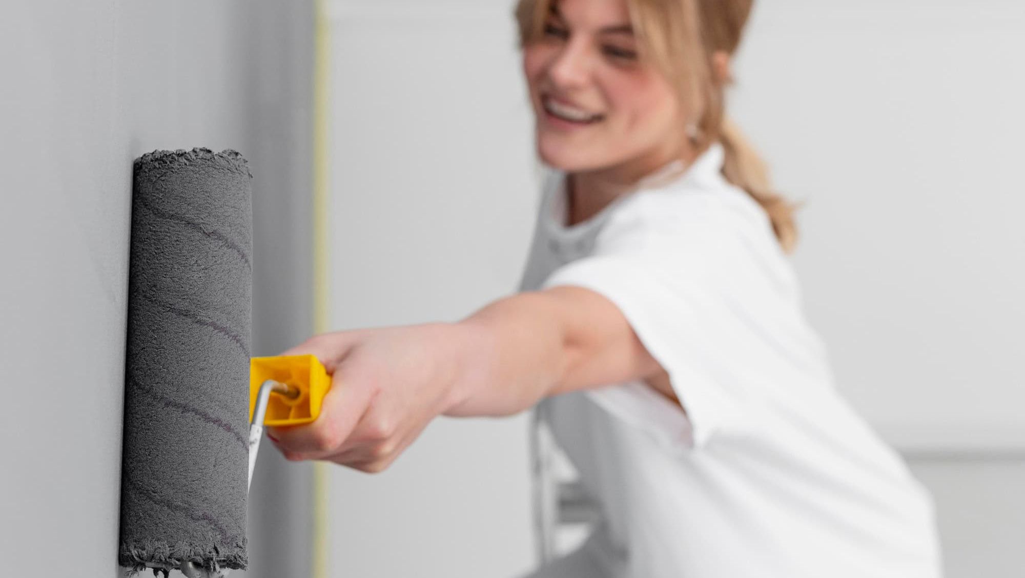 Kvinne maler en innendørs vegg med mørkegrå maling ved hjelp av malerull i godt lys.