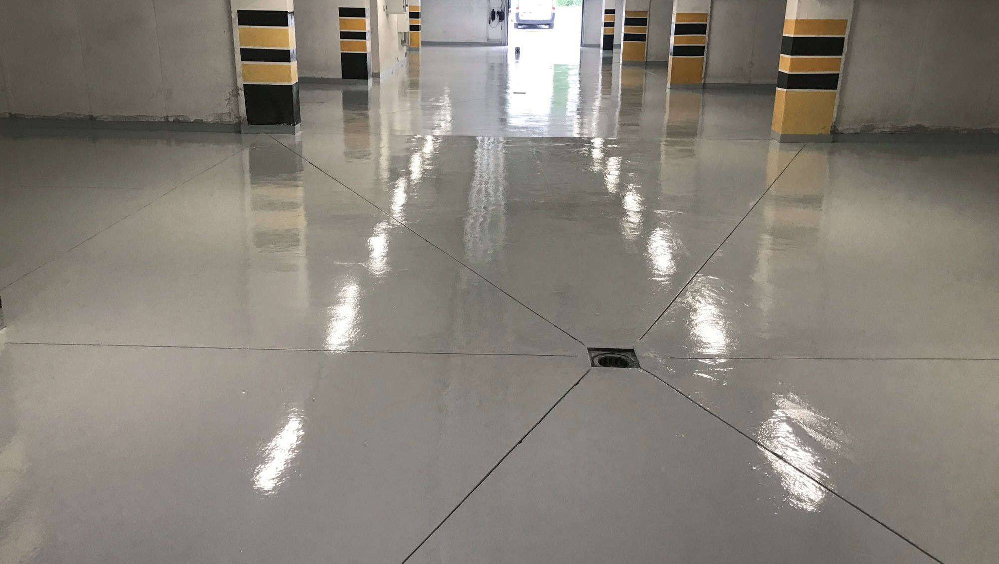 Nybehandlet garasje med blankt epoksybelagt gulv, gul-svarte søyler og sterke taklys.